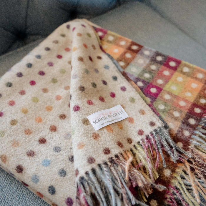 Close up of a beige polka dot blanket with fringes and a colourful checkerboard reverse displaying a Solway Blankets label on a blue couch
