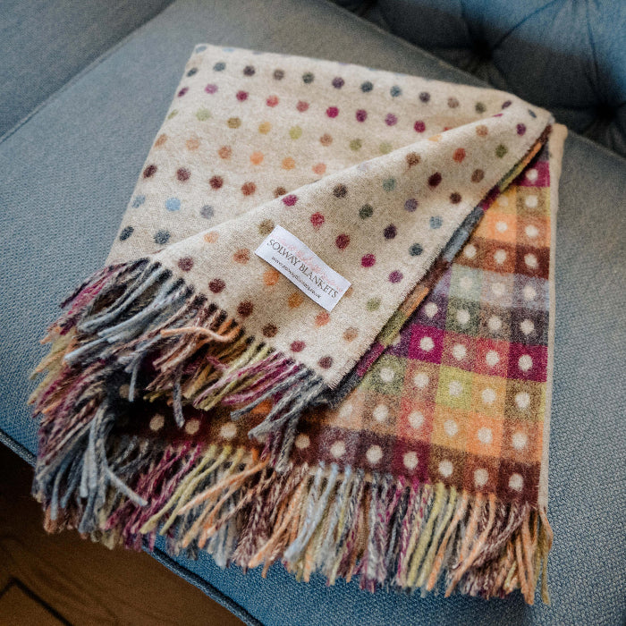 Polka dot wool blanket with colourful checkerboard reverse with fringes folded on a blue couch