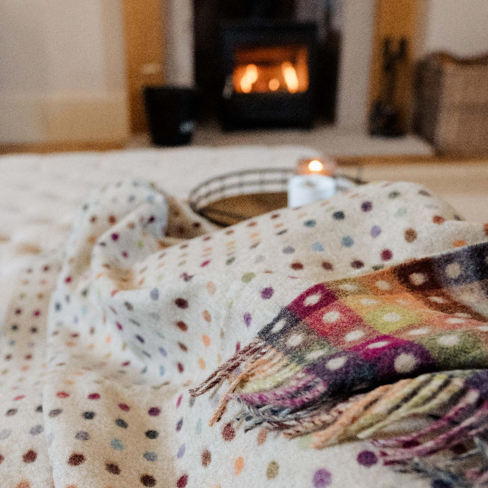 Polka dot blanket with colourful checkerboard reverse on a couch in front of a fireplace