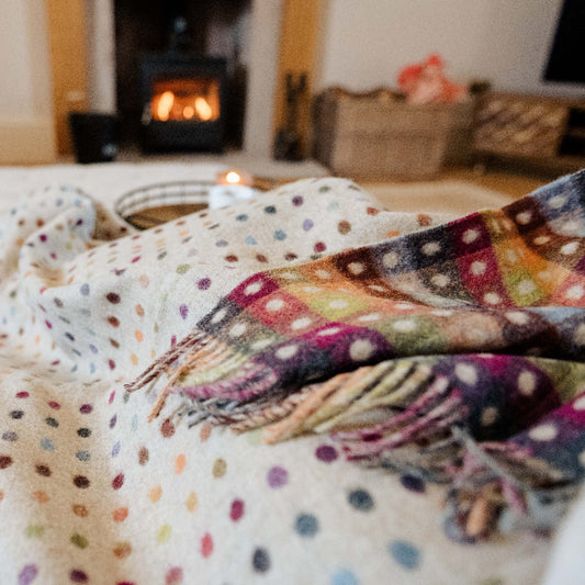 Multicoloured polka dot blanket with a checkerboard pattern on the reverse draped over a sofa with a fireplace in the background