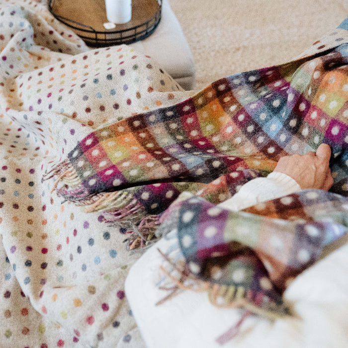Person on a couch wrapped up in a colourful polka dot blanket with a colourful checkerboard reverse