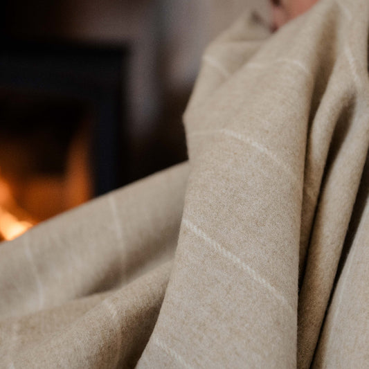 Close up of a person wrapped in a beige pinstripe blanket with a fireplace in the background