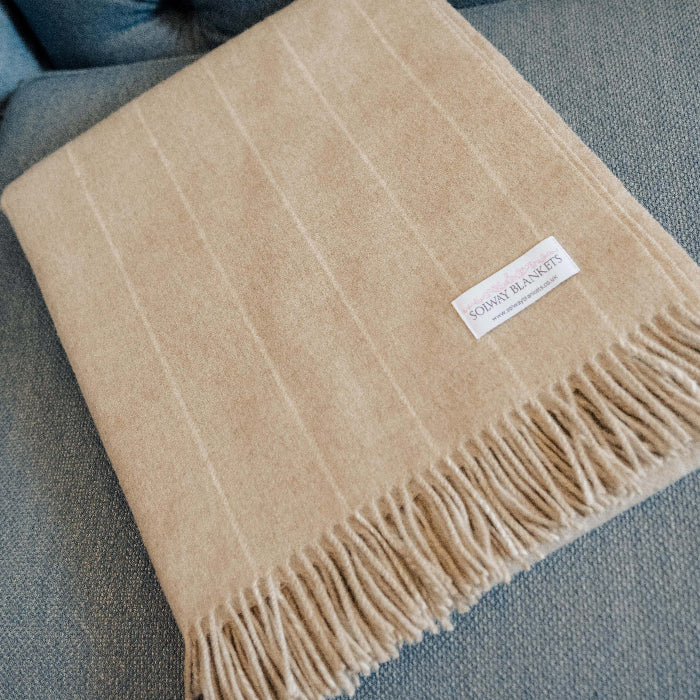 Close up of a beige pinstripe blanket neatly folded displaying a Solway Blankets label on a blue tufted sofa