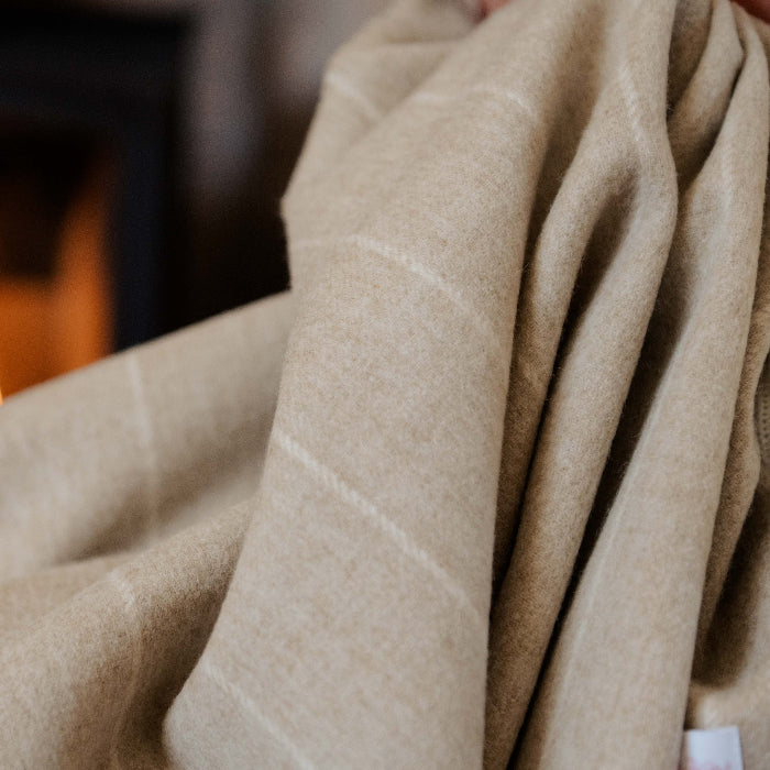 Up close image of a beige pinstripe  blanket draped over a person with a fireplace in the background
