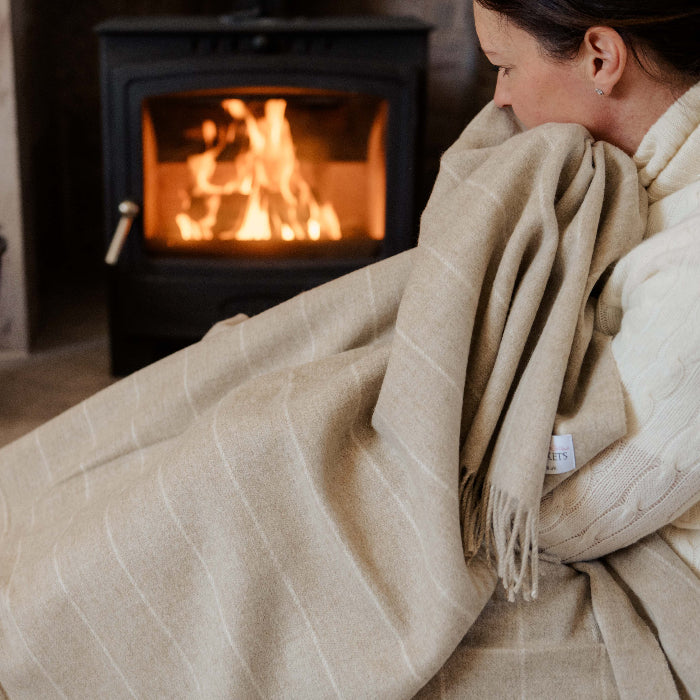 Person wrapped up in a cosy beige pinstripe blanket in front of a fireplace