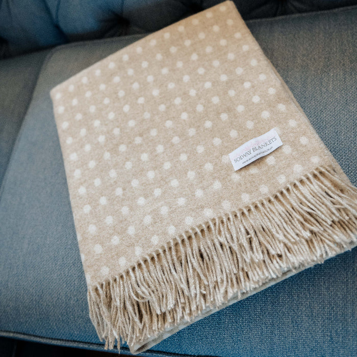 Beige and cream spot throw blanket with fringes and Solway Blankets label folded neatly on a blue tufted sofa