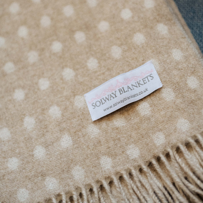 Beige and cream spotted reversible blanket with a Solway Blankets label on a blue couch
