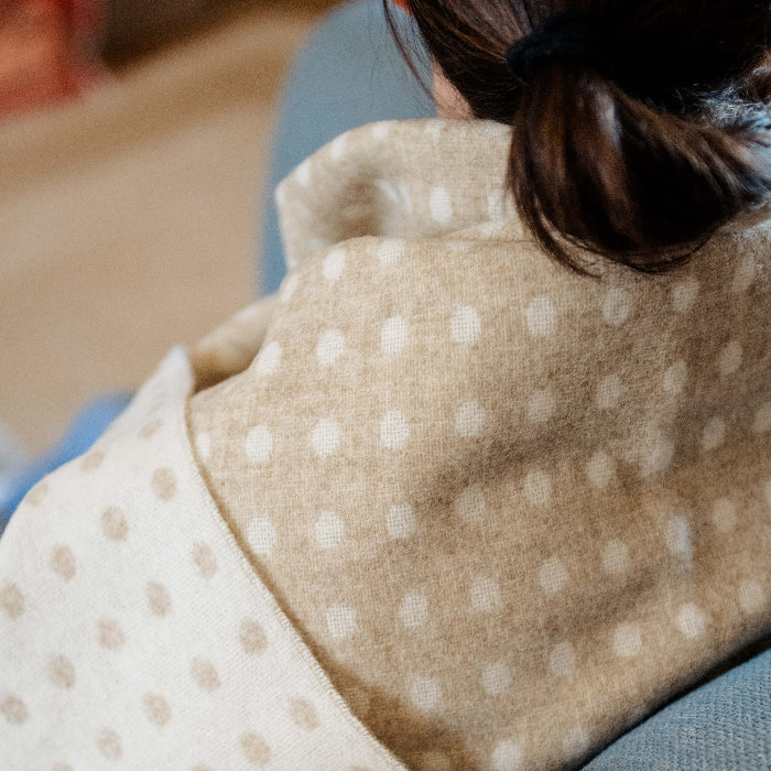 Close up of a person with a beige and cream spotted blanket wrapped around them