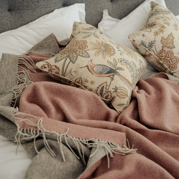 Cosy bedroom scene with patterned pillows on a white furnished bed and a pink blanket with a soft grey colour on the reverse lain on top 