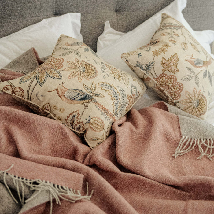 Decorative pillows with floral patterns on a grey framed bed with a pink wool throw featuring a soft grey colour on the reverse.