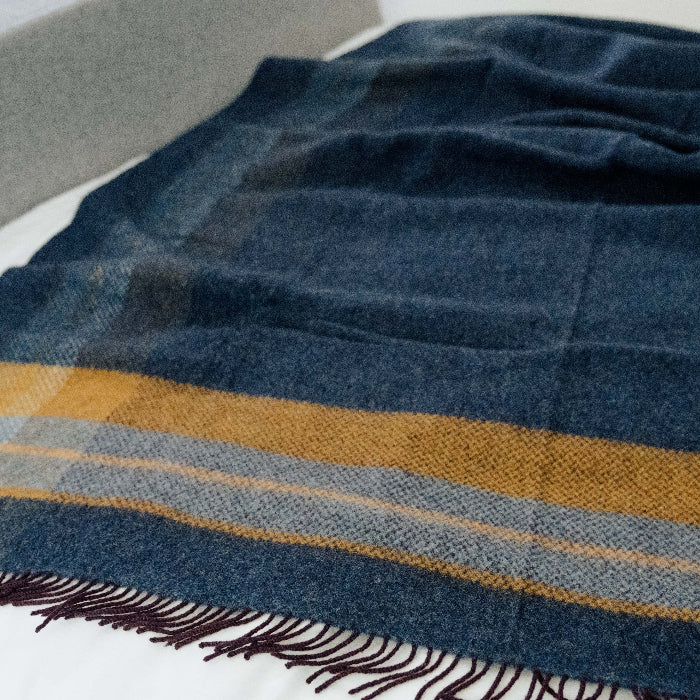 Navy blue plaid cashmere throw with mustard stripe and fringe on a white surface
