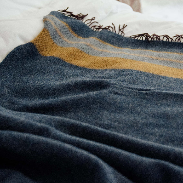 Navy blue and mustard yellow patterned throw draped over a white bed