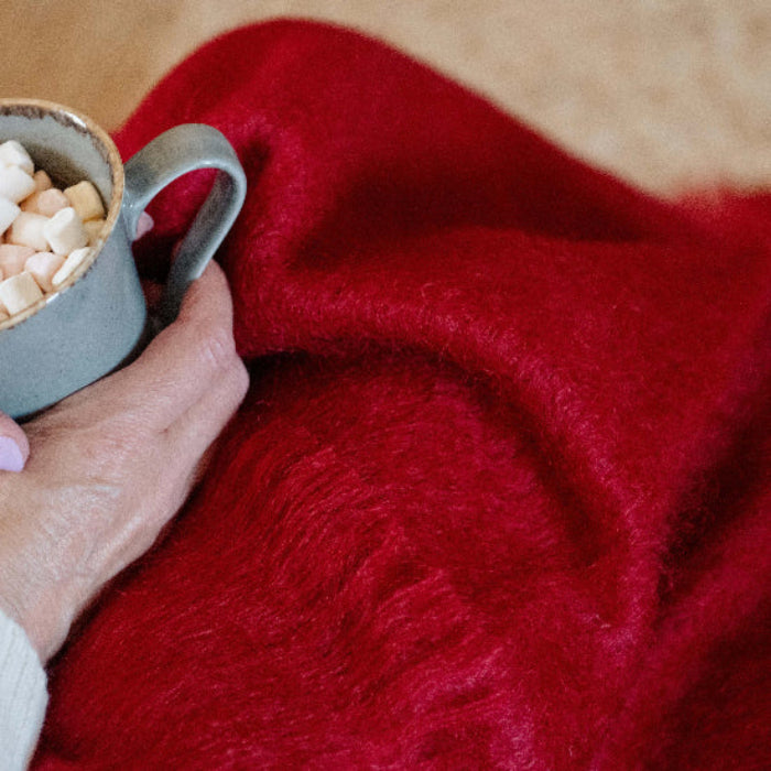 Person holding a mug of hot chocolate with marshmallows against a Berry Red Mohair Throw