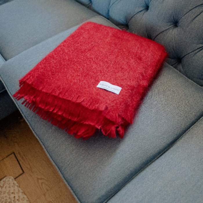 Berry Red Mohair Throw blanket on a blue sofa with a visible Solway Blankets brand label.