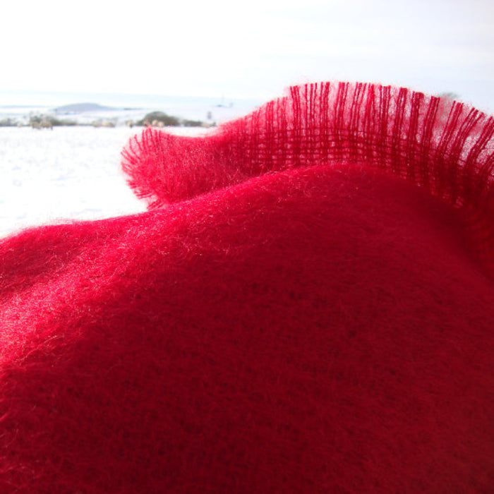 Close-up of a Berry Red Mohair Throw with a blurred snowy landscape in the background
