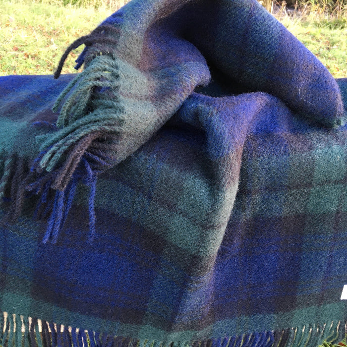 Blackwatch tartan pure wool  small knee blanket folded out with a grassy background