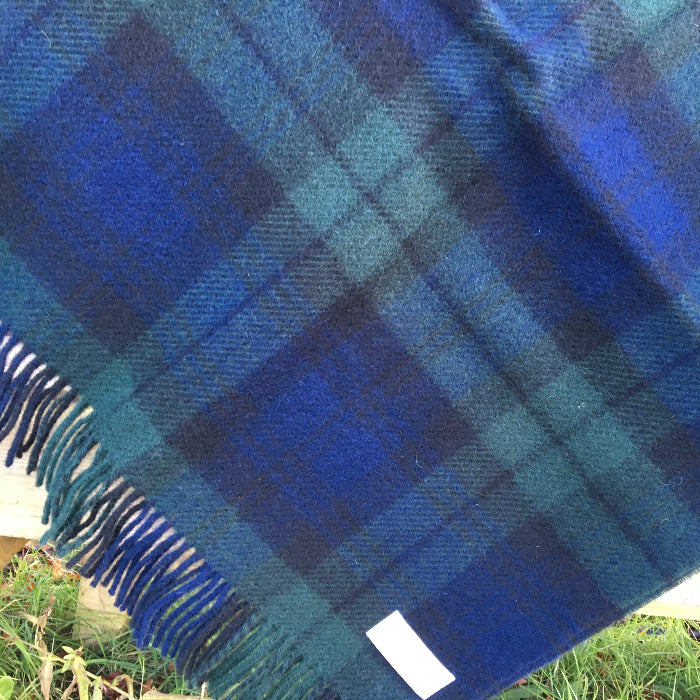 Blue and green Black Watch tartan wool knee blanket with fringe, folded out over a grassy background