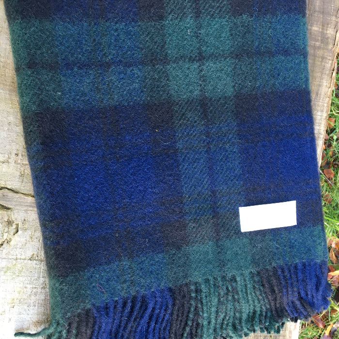 Blue and green Black Watch tartan wool blanket with fringes folded against a wooden background