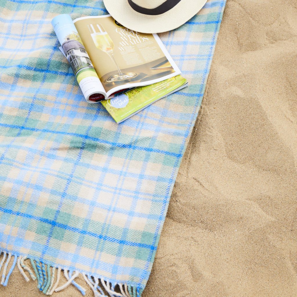Blue cottage picnic plaid waterproof blanket on sand with a hat, magazine and bottle.