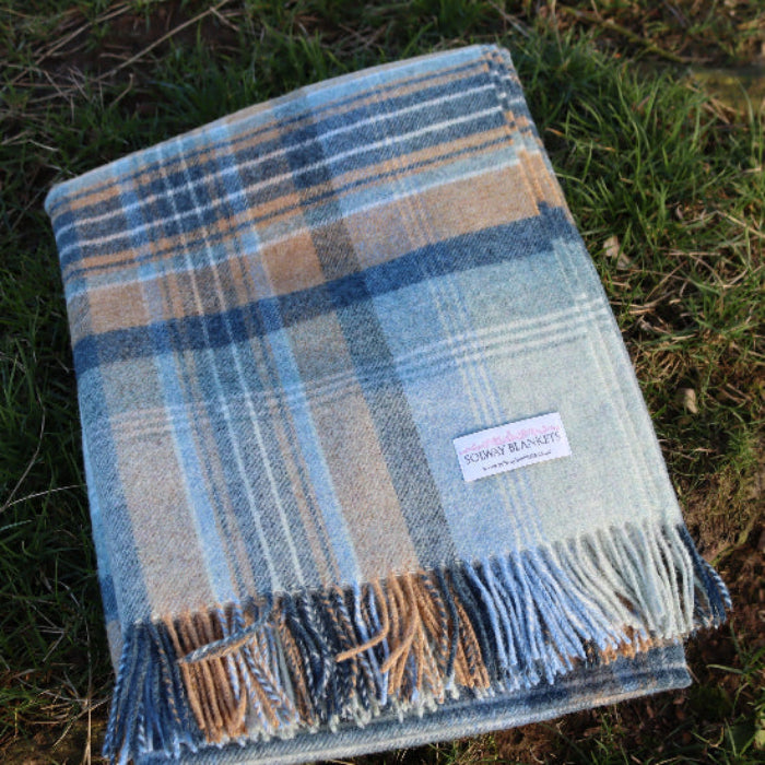 Blue Kintyre Check Shetland Wool Throw Plaid blanket with fringes on grass, featuring a brand label.