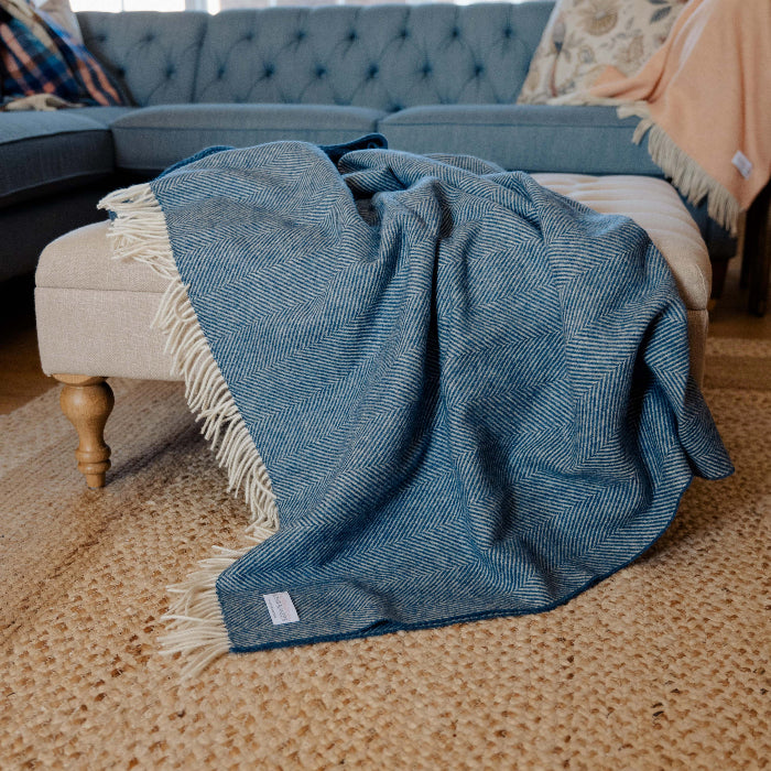 Blueberry Swirl Shetland Wool Herringbone Blanket Blue throw blanket on a beige ottoman in a living room setting.