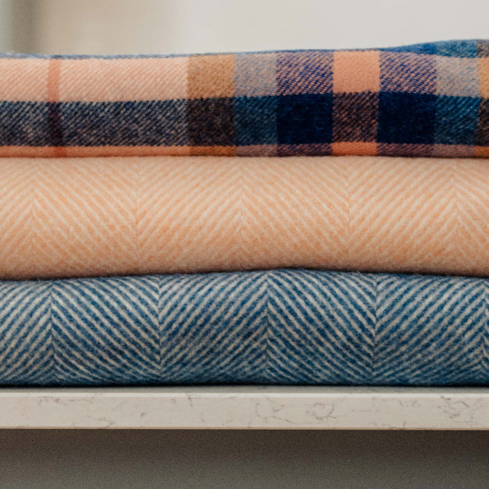 Stack of co-ordinating Shetland Wool blankets, Blueberry Swirl and Mango Sorbet herringbone and Falmouth Ivory Blue Check.  Various patterns on a neutral background