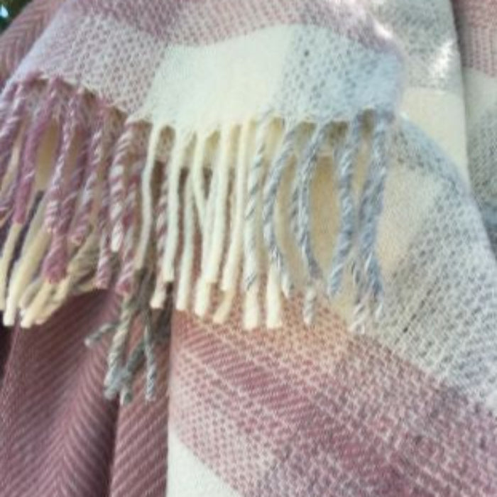 Close up of a plaid blanket with fringes in pink, cream, and grey colours.