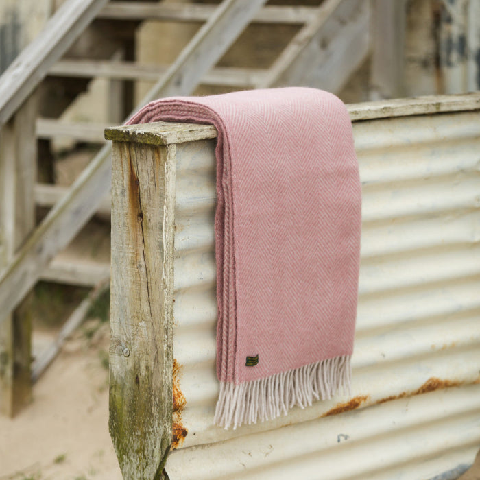 Pink and white herringbone wool blanket draped over a corrugated metal surface with wooden steps in the background.