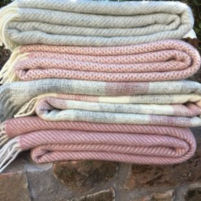 Stack of pink and white woolen blankets on a stone surface with greenery in the background