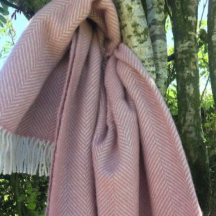 Pink and white wool blanket in a herringbone style draped over a tree branch with a natural background