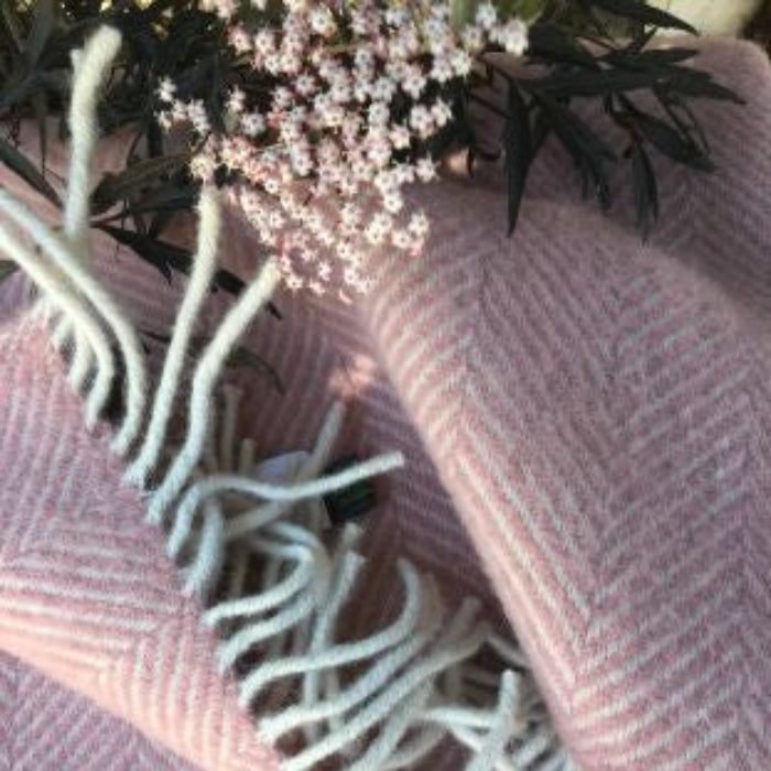 Pink and white plaid herringbone style blanket with white fringe with small flowers laid on top