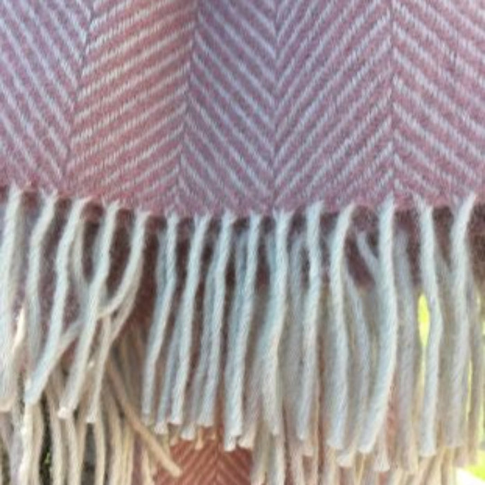 Close up of a pink and white herringbone patterned wool blanket with white fringe.