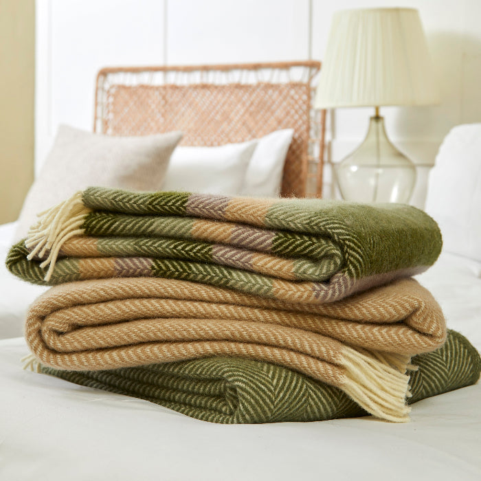 Stack of green, yellow and beige plaid wool blankets on a bed with a lamp and headboard in the background.