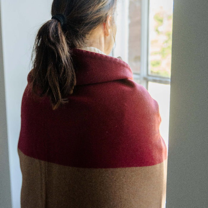 Person wrapped up in a burgundy red and tan cashmere blanket throw gazing out of a window