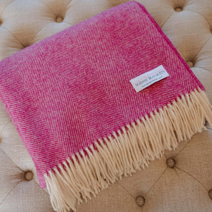 Folded Bright Pink Herringbone Shetland Wool Blanket with cream fringe on a tufted beige surface