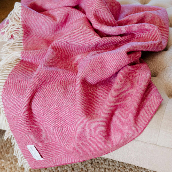 Bright Pink Herringbone Shetland Wool Blanket draped over a beige ottoman on a carpeted floor.