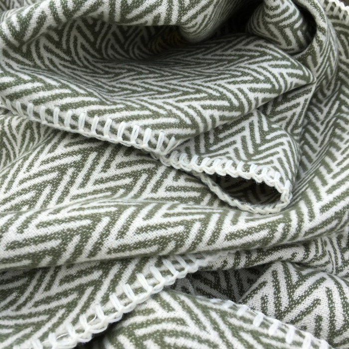 A close-up of folded fabric with a mineral green and white herringbone pattern and a white blanket stitch trim.