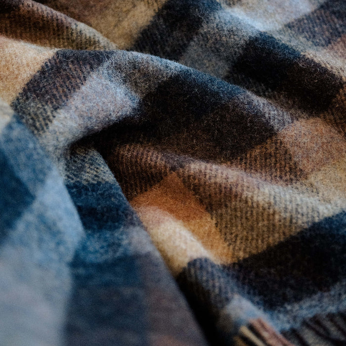 Close up of a plaid wool blanket with colours of blue, navy, tan and chocolate. 