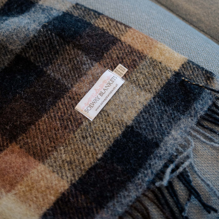 Plaid wool blanket with a Solway Blankets label folded on top of a blue couch