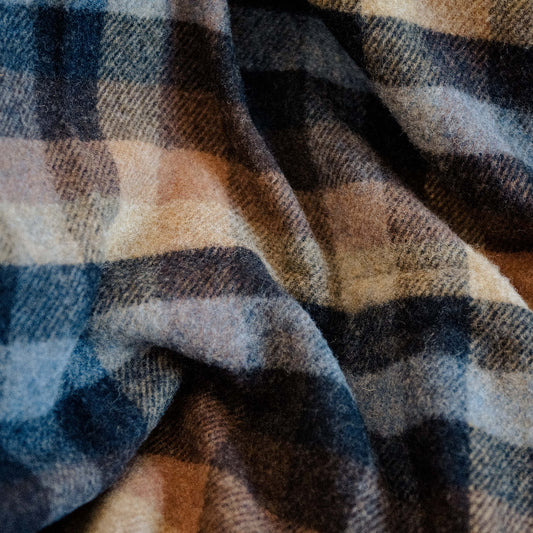 Close up of plaid wool blanket with blue, navy, tan and chocolate colours. 