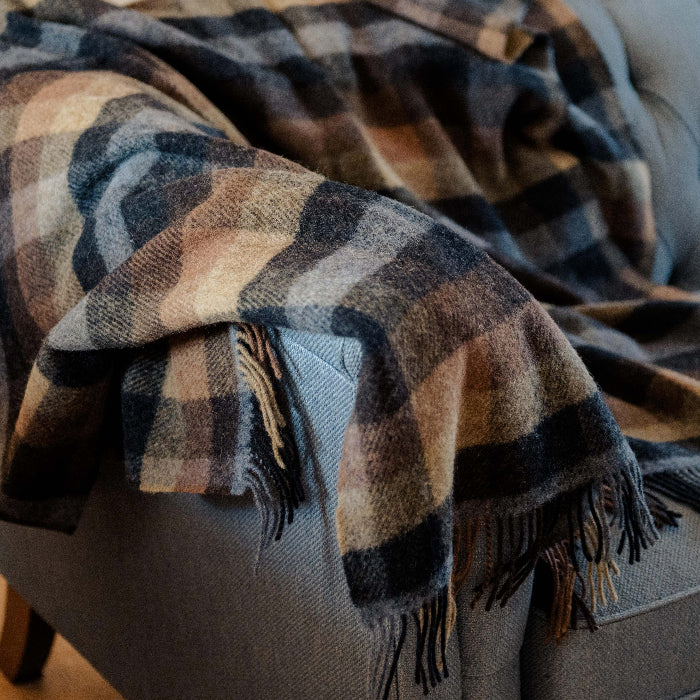 Plaid wool blanket with fringe draped over a grey sofa
