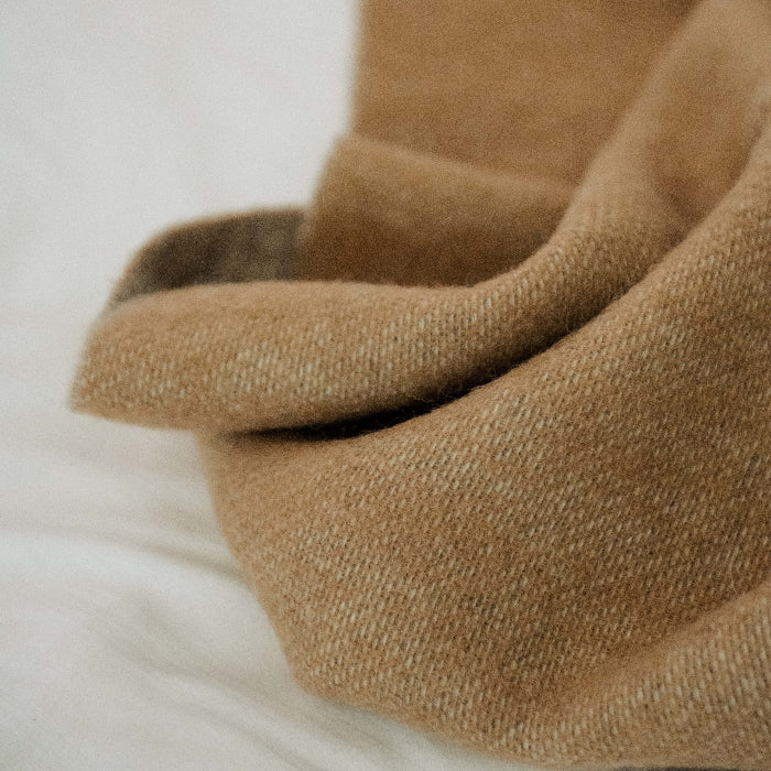 Close up of an earthy brown wool blanket on a bed with white furnishings
