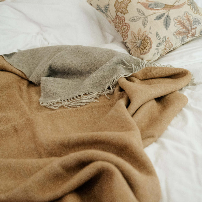 Woollen brown blanket with a soft grey on the reverse, patterned pillows on a bed with white bedding