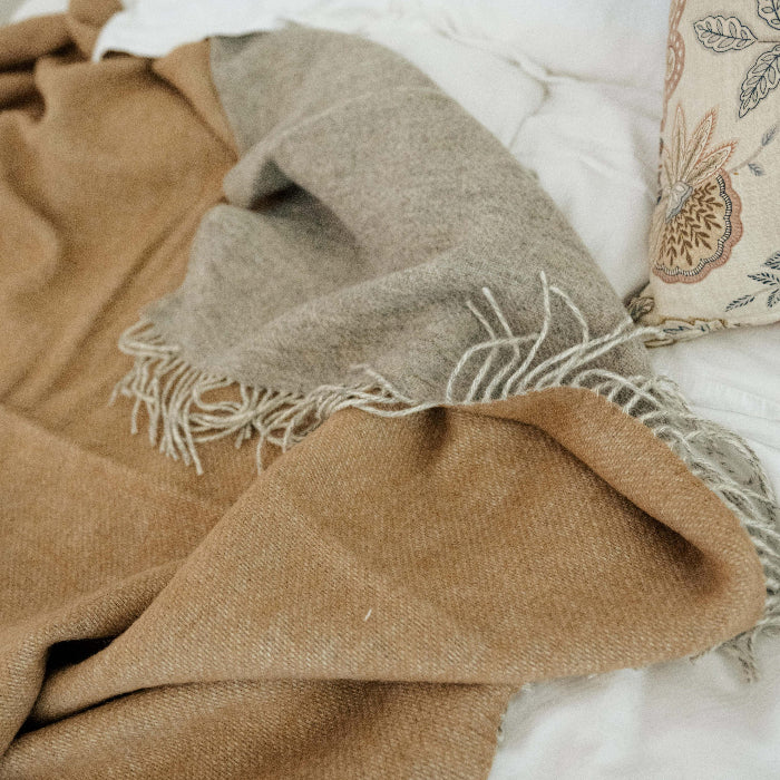 Brown wool throw with a soft grey colour on the reverse, placed on a bed with white furnishings