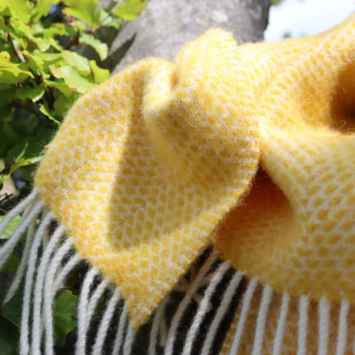 Close up of a yellow textured wool blanket with white fringe against a natural background