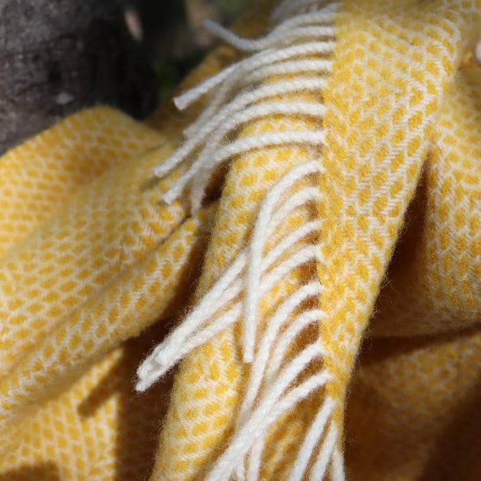 Close up of a yellow woven wool fabric blanket with white fringe