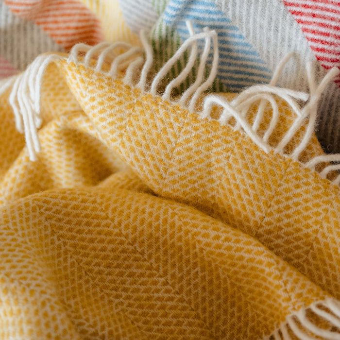 Close up of a yellow woven fabric blanket with fringe against a colourful material. 