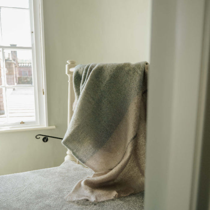The Celadon Mohair Throw blanket draped over a stair bannister it in a room with a window over looking a castle