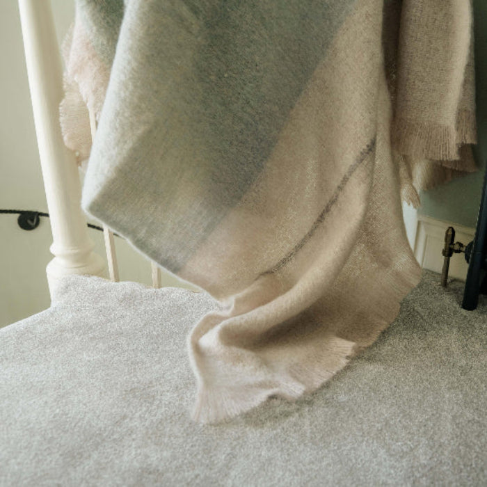 Celadon Mohair Throw a striped Blanket in pale green and off whites draped over a bannister next to a radiator in a room.