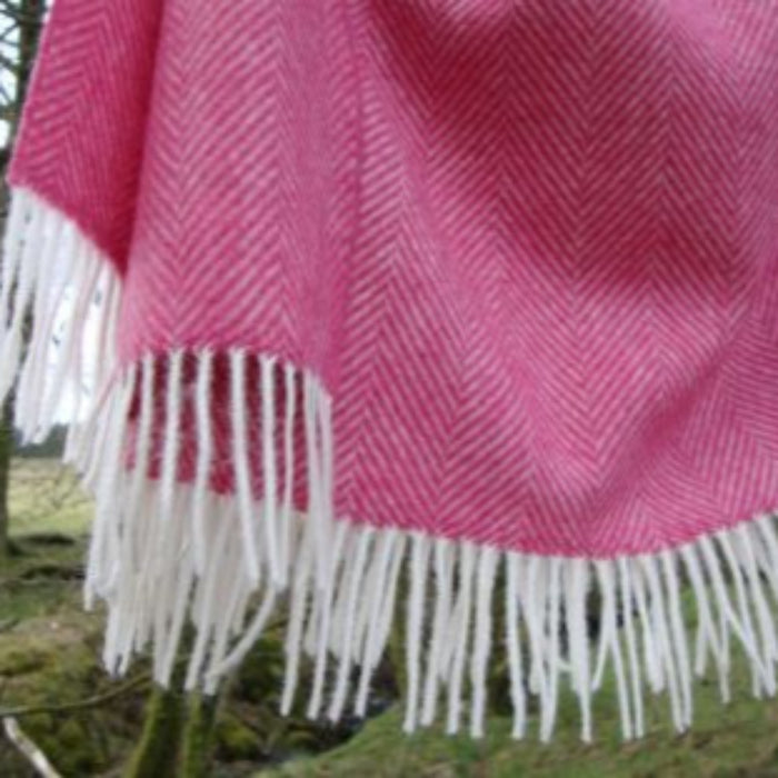 Pink woven herringbone patterned blanket throw with white fringe in a natural background